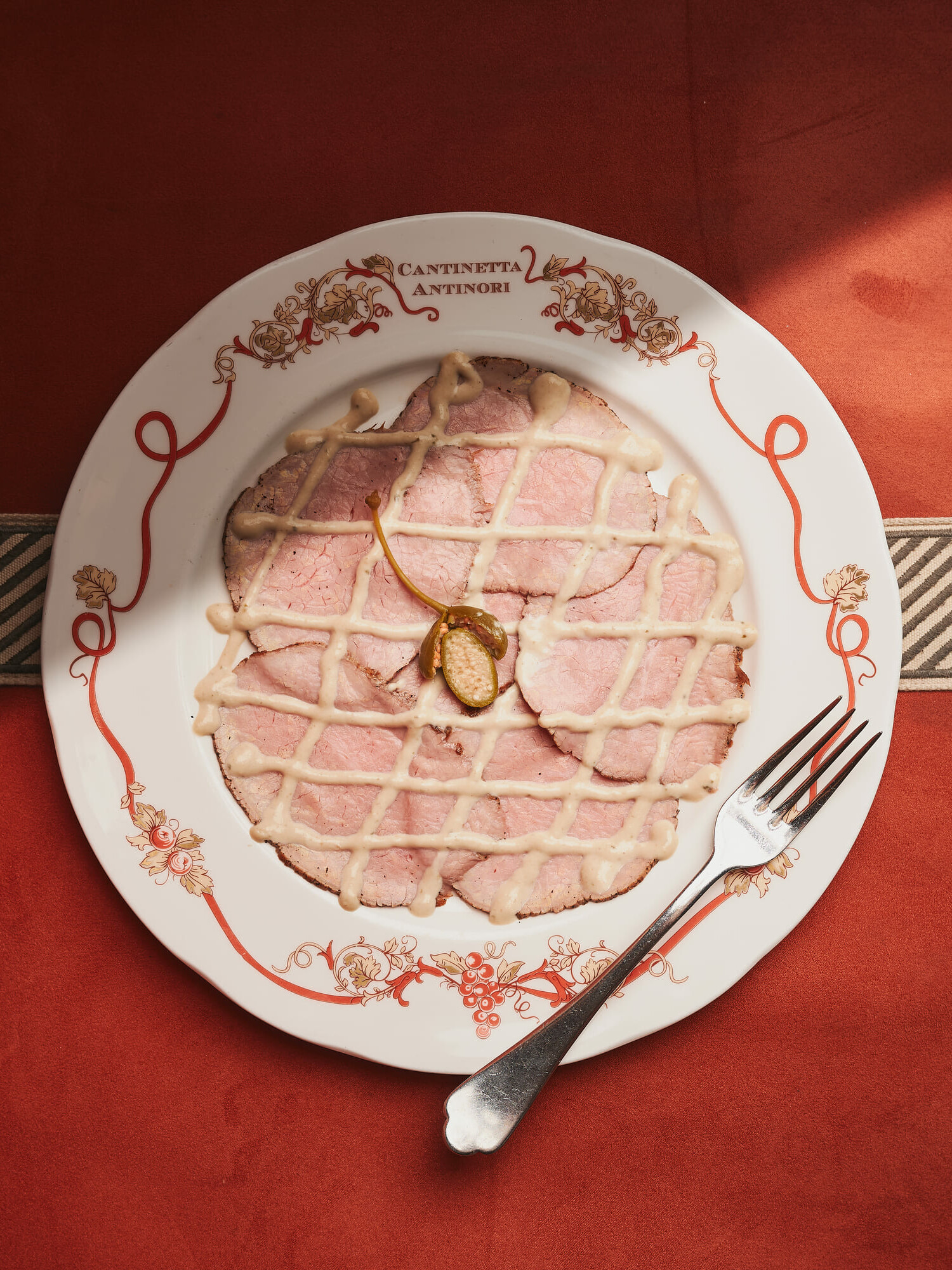 Vitello tonnato with tuna sauce and a caper berry, served on a Cantinetta Antinori plate